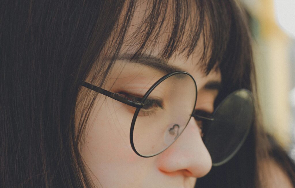 A detailed close-up shot of a young woman wearing round glasses. Soft lighting enhances her serene expression.