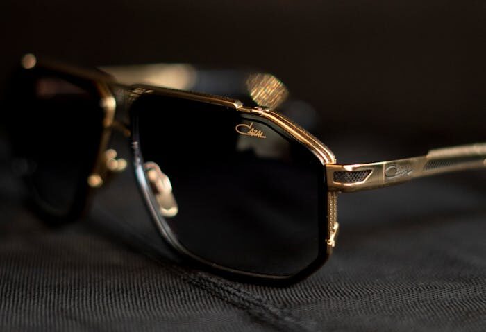 Elegant gold-rimmed sunglasses displayed on a dark cloth with soft lighting.